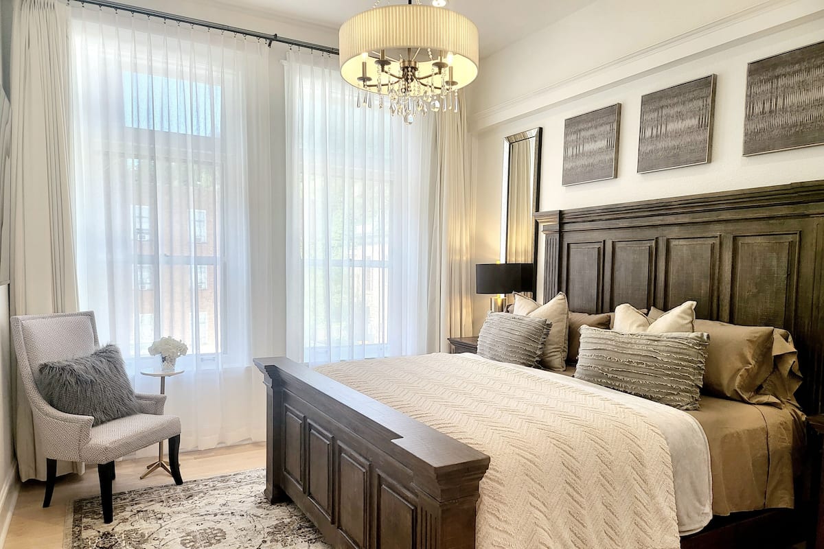 Une chambre à coucher avec un grand lit, une chaise, une petite table ornée de fleurs et un lustre.