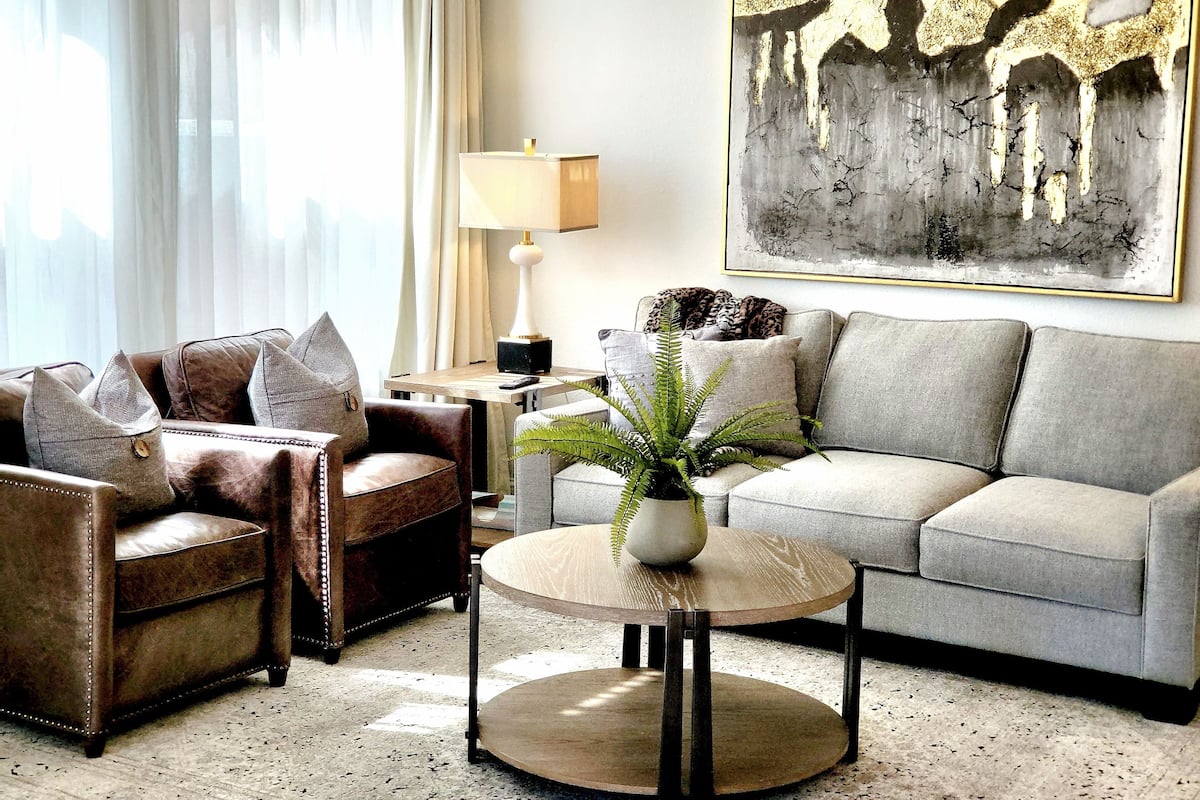 Un salon avec un canapé, un fauteuil, une table basse et un tableau accroché au mur.