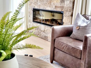 Un salon avec une cheminée en pierre, un canapé en cuir et une fougère en pot.