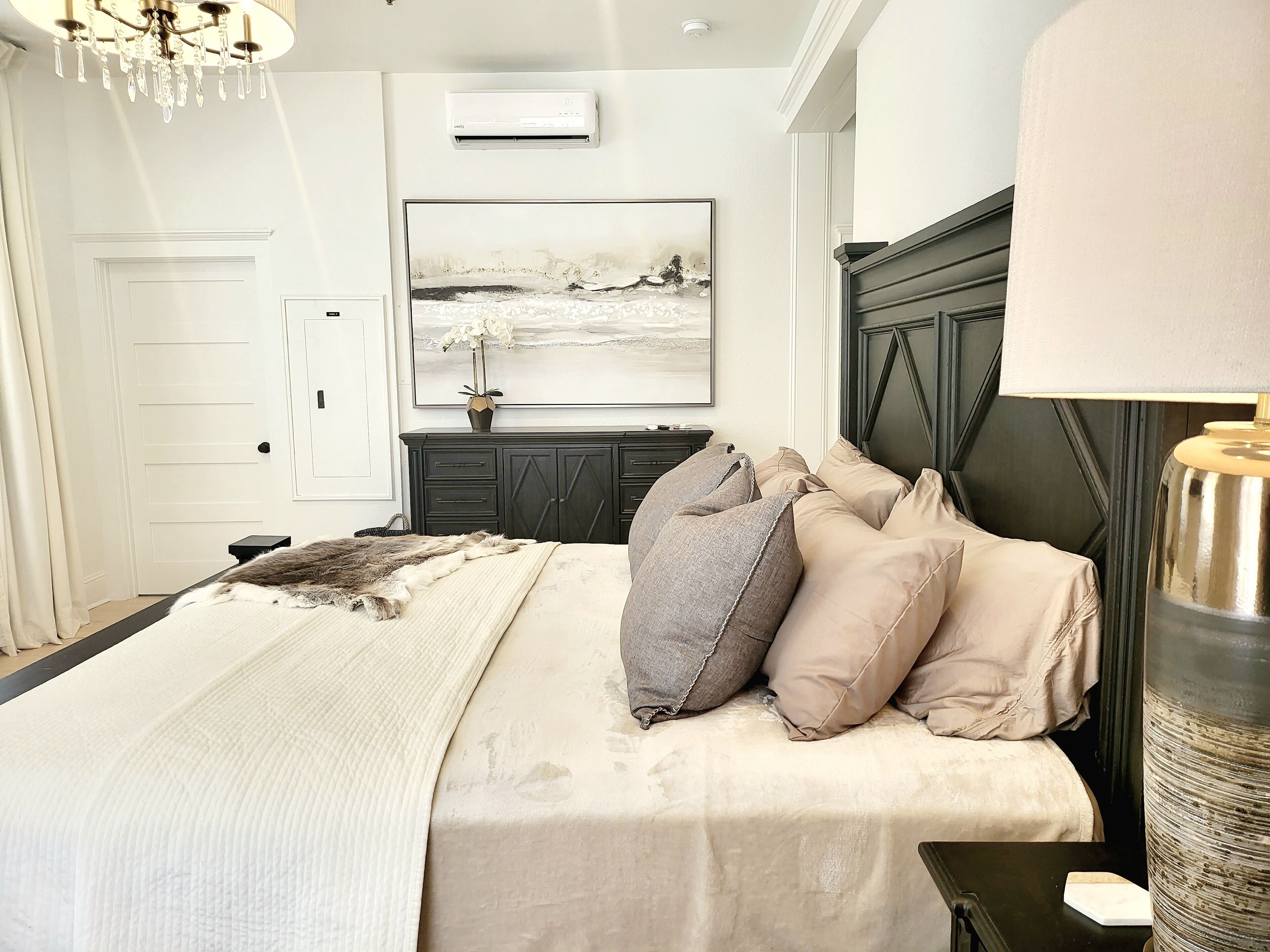Une chambre à coucher avec un lit, un lustre, un tableau, une commode et une lampe.