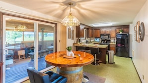 A kitchen with a wooden barrel table, a dining area with chairs, and a sliding glass door leading to an outdoor deck. - Close to Coquille River, Bandon Dunes, centrally located in the county -hot tub! (Coquille)