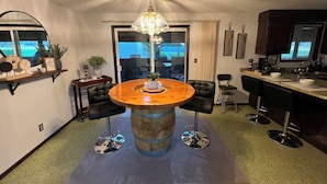 A modern kitchen with a central island, black bar stools, a chandelier, and a view through the glass door. - Close to Coquille River, Bandon Dunes, centrally located in the county -hot tub! (Coquille)
