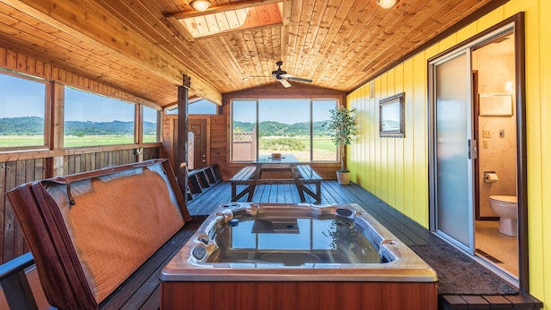 A wooden cabin with a hot tub, wooden deck, and large windows offering a view of the outdoors. - Close to Coquille River, Bandon Dunes, centrally located in the county -hot tub! (Coquille)