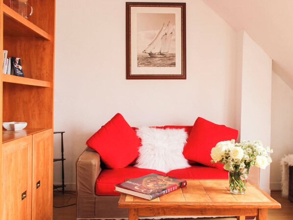 Un salon avec un canapé rouge, un meuble en bois, un tableau encadré au mur et une table sur laquelle se trouvent un livre et un vase de fleurs.
