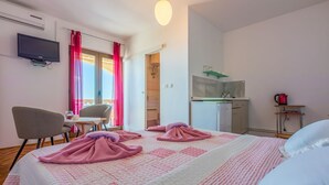Ein Hotelzimmer mit Bett, Schreibtisch, Stuhl, Fernseher, einer Küchenzeile und einem Badezimmer.