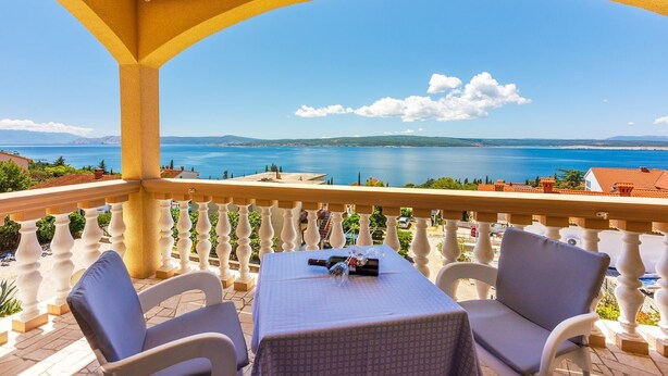 Ein Balkon mit Tisch und Stühlen mit Blick auf eine malerische Meereslandschaft und sanfte Hügel in der Ferne.