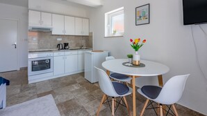 A modern kitchen with white cabinets, a built-in oven, and a coffee maker. There is a dining area with a white table and four chairs. - Sea view accommodation 300 metres to the beach (Dramalj)