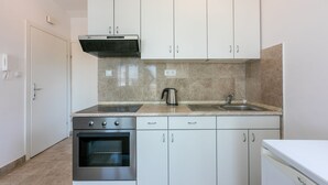 A modern kitchen with white cabinets, a stainless steel oven, a kettle, and a dishwasher. - Studio flat with sea view (Dramalj)