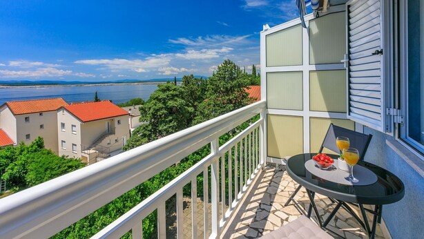 A balcony with a table and chairs, overlooking a body of water and buildings. - Studio flat with sea view (Dramalj)