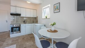 A modern kitchen with white cabinets, a built-in oven, and a dining area with a round table and two chairs. - Studio flat with sea view (Dramalj)
