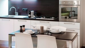 Eine moderne Küche mit weißen Schränken, einem Edelstahlbackofen und einem Essbereich mit einem Tisch für zwei Personen.