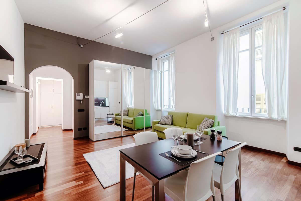 A modern living room with a dining area, green sofa, and a kitchen in the background.