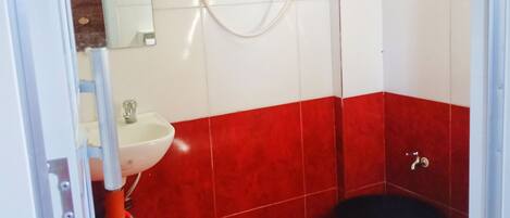 A bathroom with red and white tiles, a white sink, a black toilet, and a shower unit.
