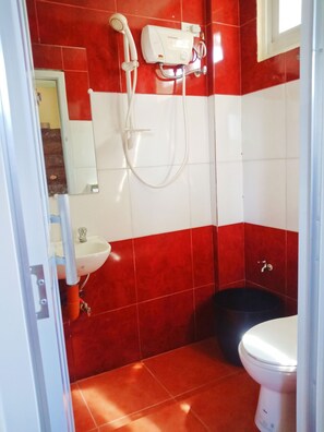 A bathroom with red and white tiles, a white sink, a black toilet, and a shower unit.