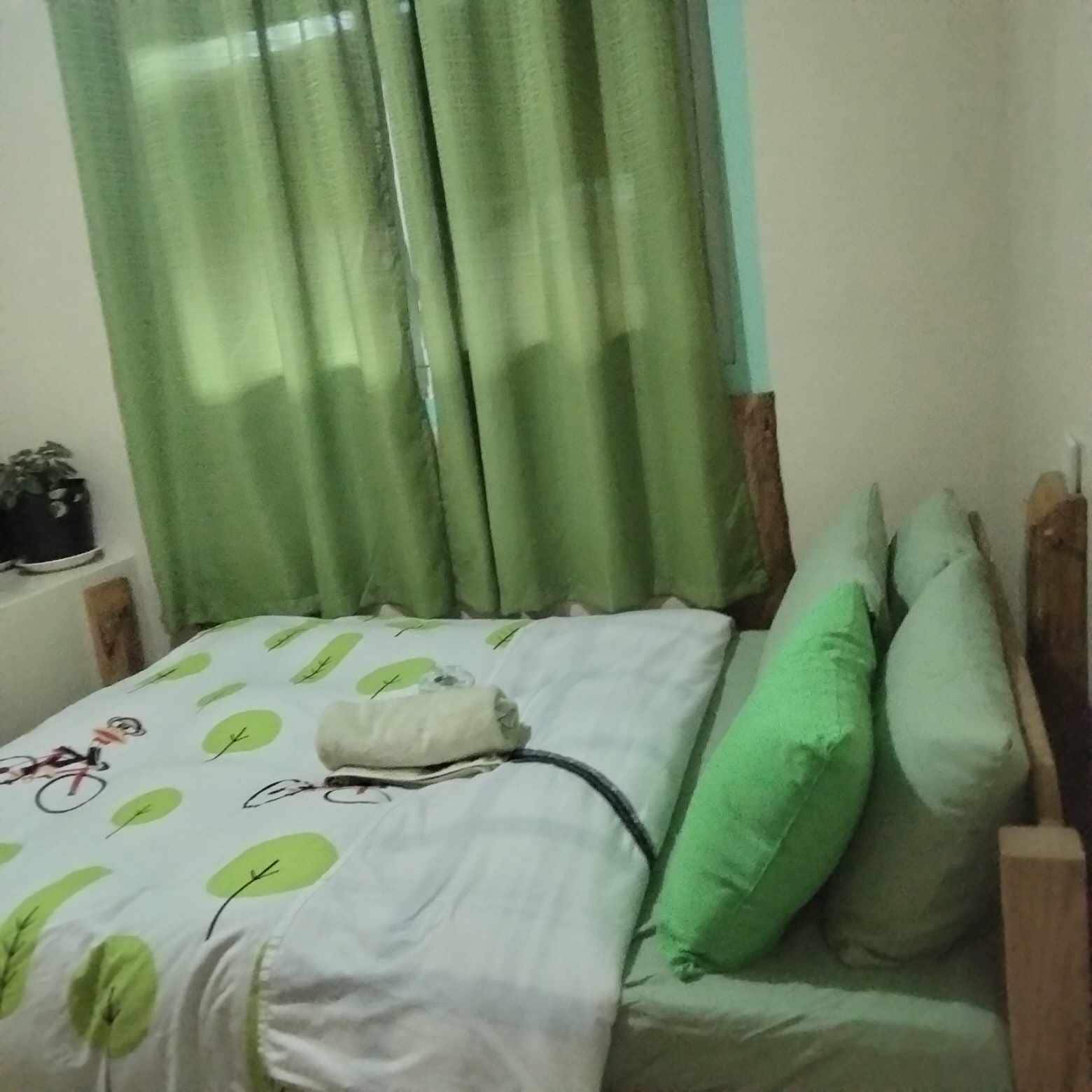 A bed with green pillows, a white bedspread with leaf patterns, and a window with green curtains.