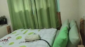 Uma cama com almofadas verdes, um cobreleito branco com motivos de folhas e uma janela com cortinas verdes.