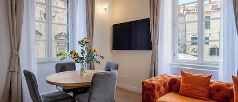 Moderni olohuone, jossa on ruokailutila, sohva ja seinälle asennettu televisio.