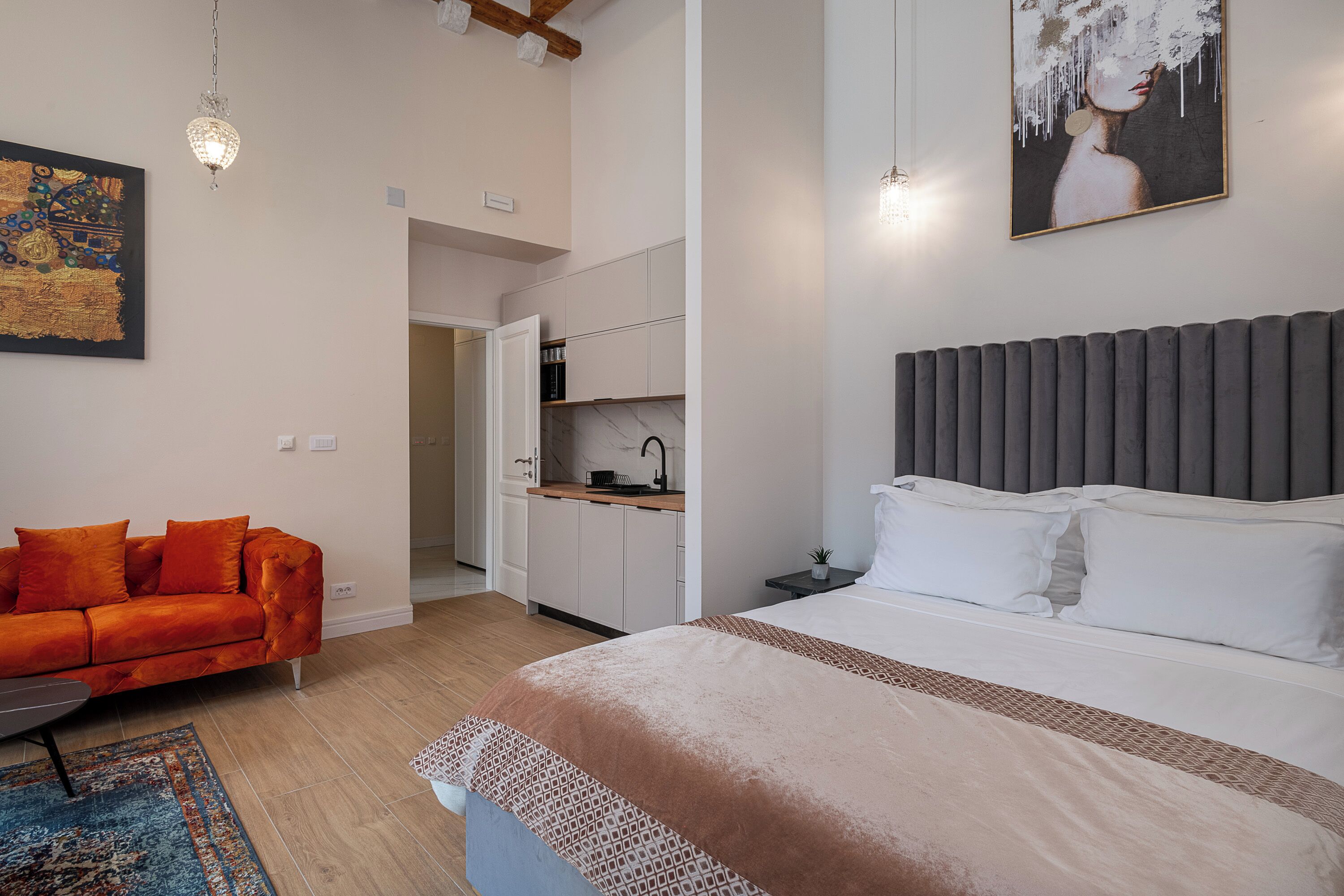 A modern bedroom with a bed, a sofa, a kitchen area, and a hallway.