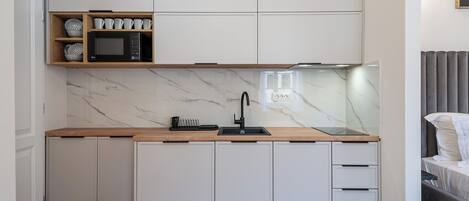 A modern kitchen with white cabinetry, a wooden countertop, a built-in microwave, and a sink.