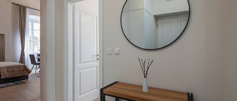Una habitación de hotel con una mesa consola de madera, un espejo redondo y un jarrón con flores.