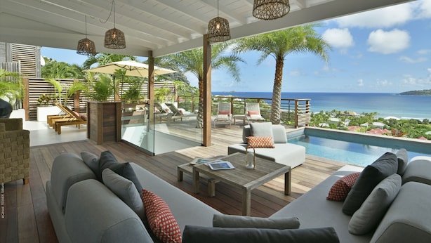 A modern outdoor lounge area with a pool, wooden furniture, and a view of the ocean. - Villa Nagabaaja  (St. Barthelemy)
