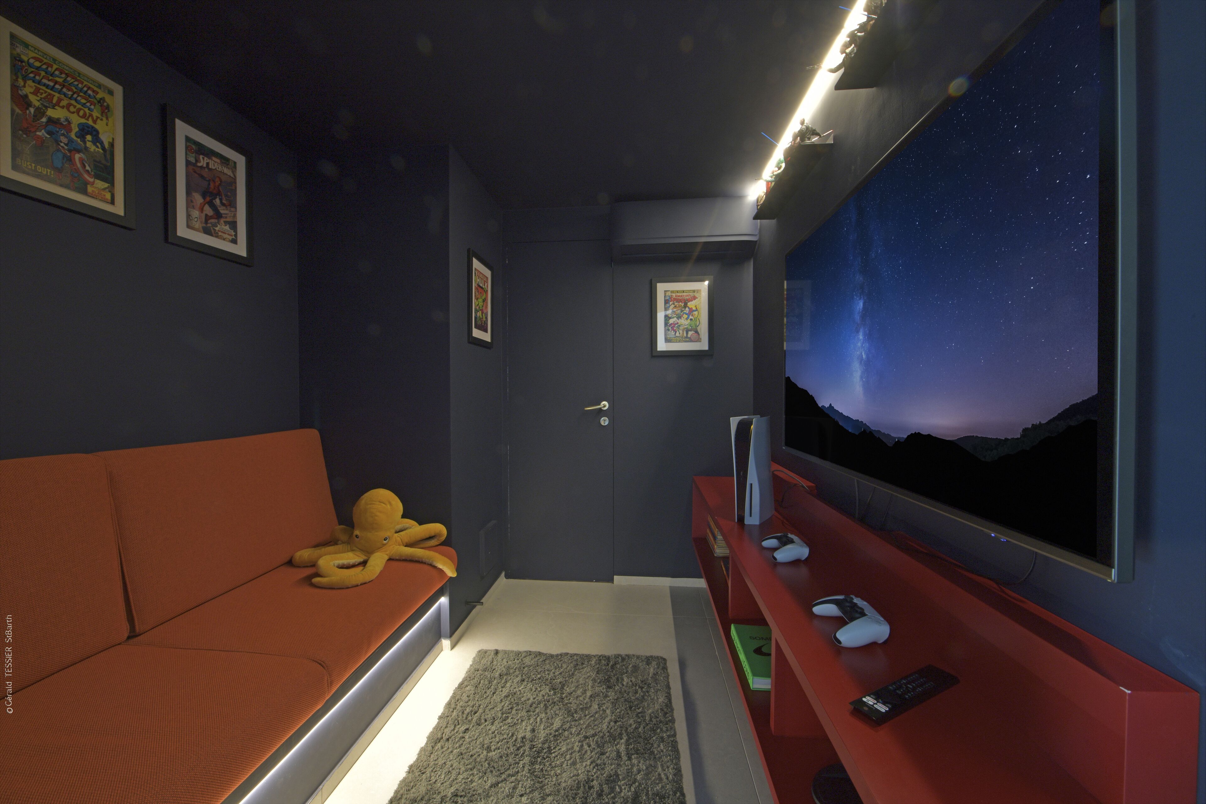 Une pièce avec un mur bleu foncé, un canapé rouge, un grand téléviseur fixé au mur et une porte avec une clé dans la serrure.