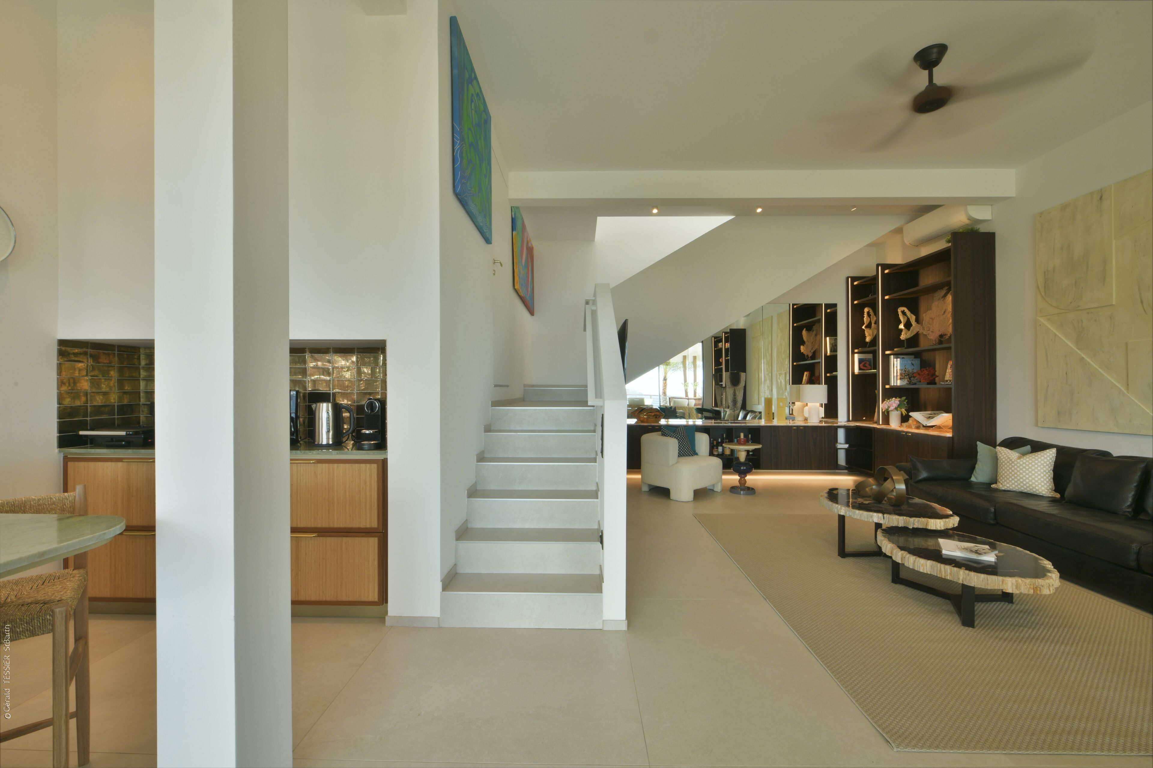 Amplia sala de estar con una escalera que lleva a una cocina, un comedor y una zona de estar con sofá y mesa de centro.