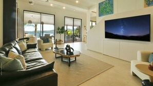 A modern living room with a leather sofa, a coffee table, and a large flat-screen TV mounted on the wall. - Villa Nagabaaja  (St. Barthelemy)