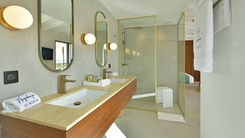 Un baño moderno con tocador de madera, dos lavamanos, un espejo grande y ducha con mampara de vidrio.