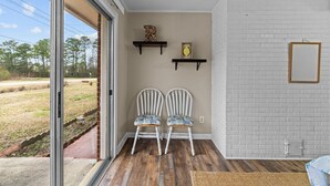 Una habitació amb dues cadires blanques, un terra de fusta, una paret de maó blanc i una porta de vidre que dona a l'exterior.