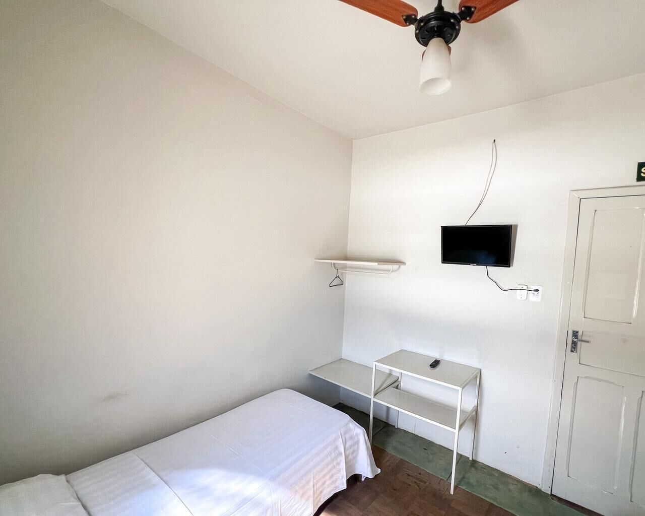 Een kleine, schone kamer met een bed, een bureau, een televisie en een deur.