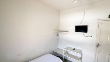 Ein kleiner, sauberer Raum mit einem Bett, einem Schreibtisch, einem Fernseher und einer Tür.