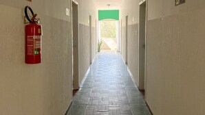 A hallway with a fire extinguisher mounted on the wall, doors on both sides, and a green exit sign. - Elite Economy Hotel (Para de Minas)