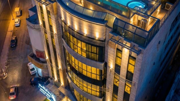 Un hotel moderno con piscina en la azotea, varios balcones y una fachada bien iluminada.