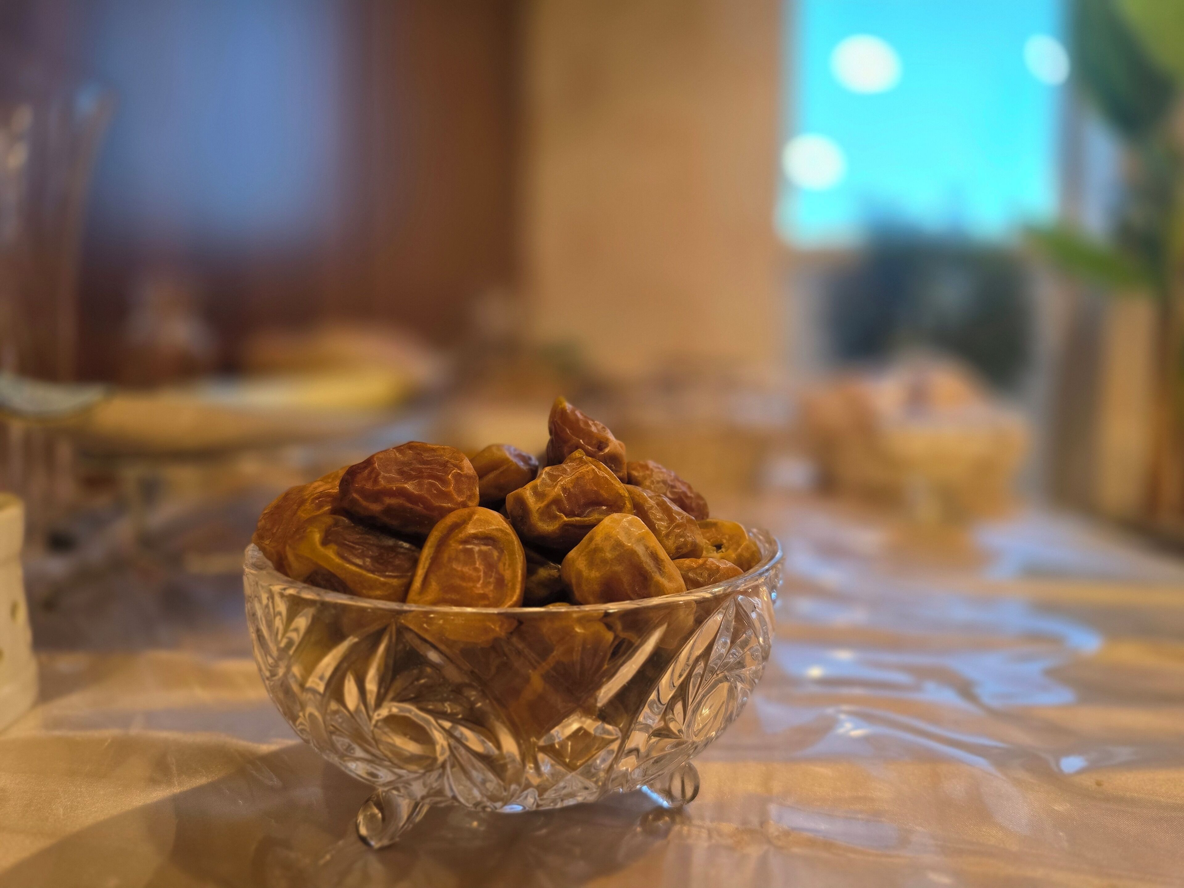 A clear glass bowl filled with dates on a tablecloth.