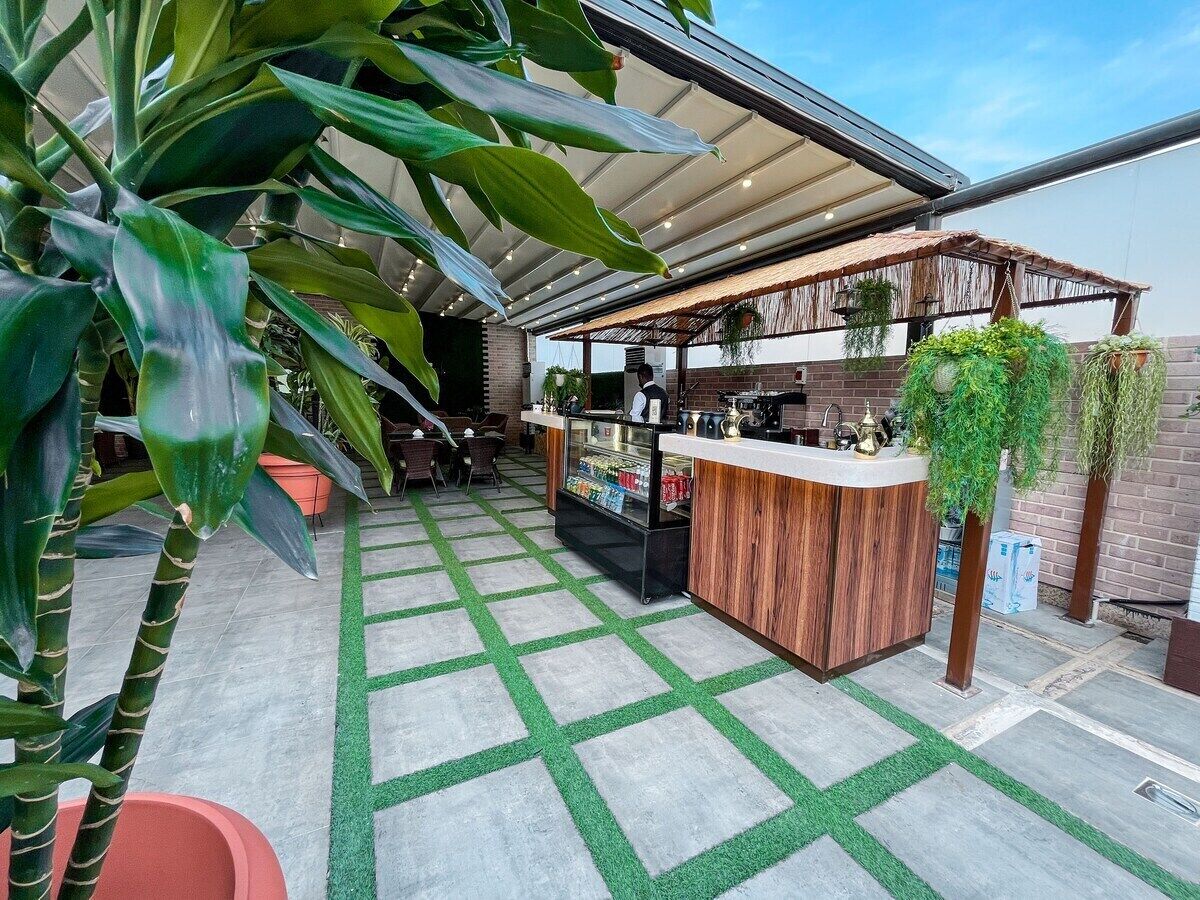 An outdoor bar area with a wooden counter, green artificial grass flooring, and potted plants.
