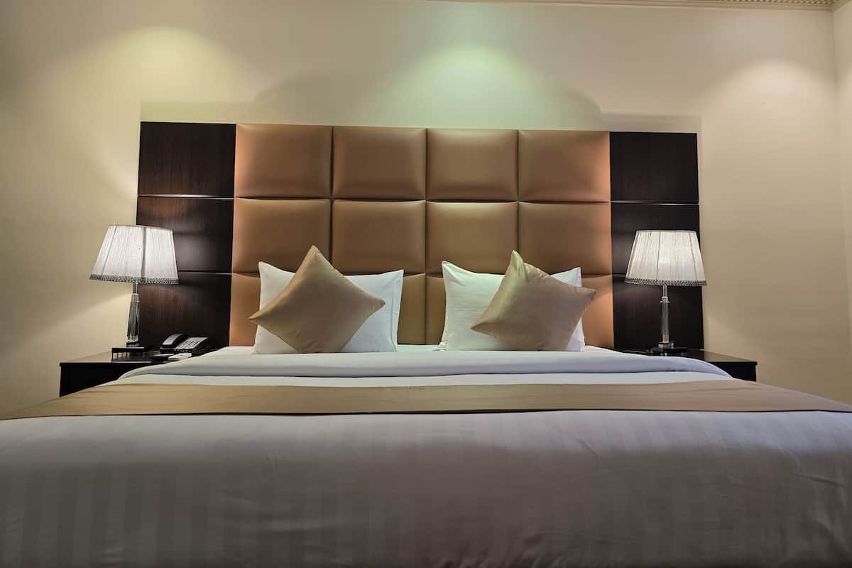 Une chambre d’hôtel avec un grand lit, deux lampes de chevet et une tête de lit rembourrée.