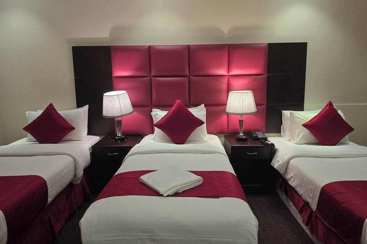 Une chambre d’hôtel avec deux lits, chacun doté d’une tête de lit rouge, de draps blancs et d’un plaid rouge. Il y a deux tables de chevet avec des lampes et un téléphone.