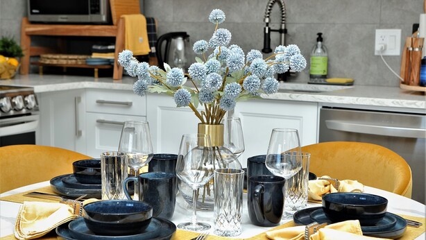 A dining table set with blue dinnerware, clear glassware, and a vase with blue flowers. - Bright and sunny 1-bdr guest suite in South Calgary (De Winton)