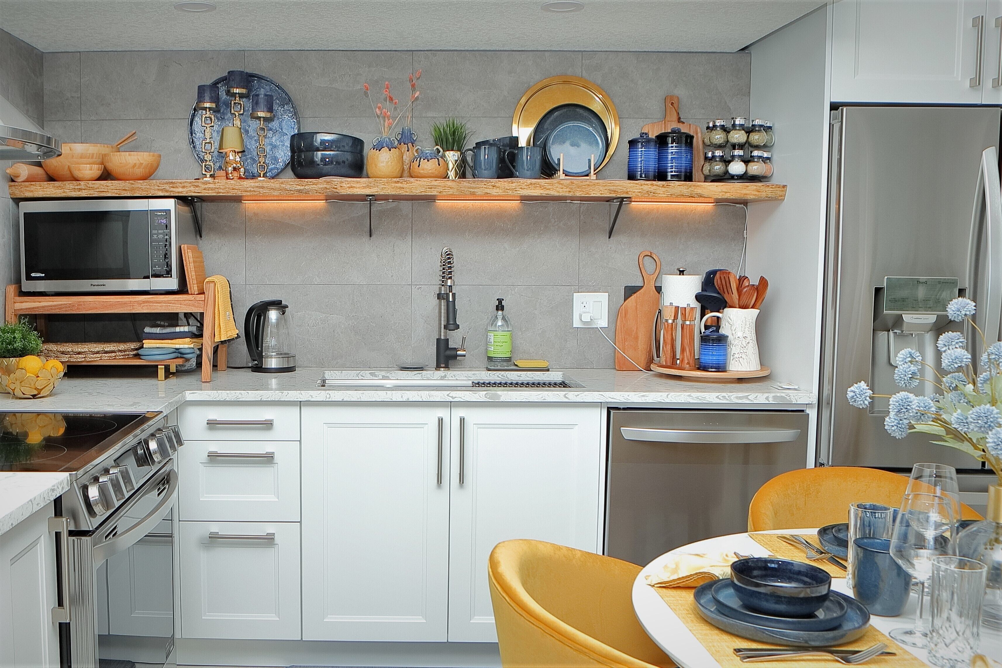 Una cocina moderna con armarios blancos, microondas, estufa y pileta. Hay una repisa de madera sobre la mesada con diversos utensilios de cocina.