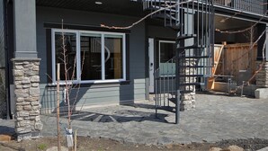 A modern two-story house with a stone pillar, a balcony, and a window overlooking a stone-paved area. - Bright and sunny 1-bdr guest suite in South Calgary (De Winton)