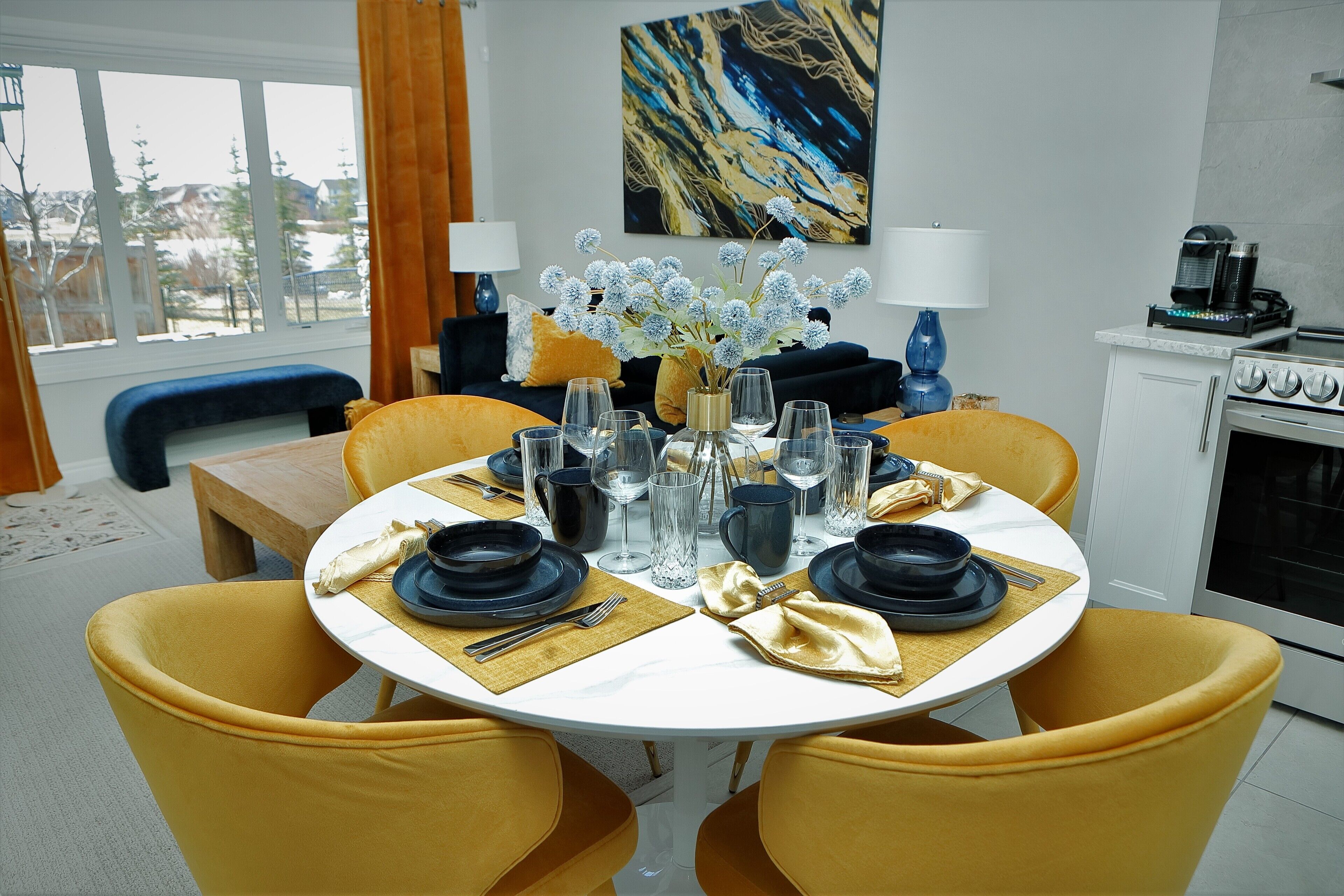 A dining area with a round table set for four, yellow chairs, and a vase of flowers.