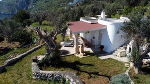 Una villa bianca con tetto rosso, circondata da alberi e un muro in pietra, con vista su un paesaggio montuoso.