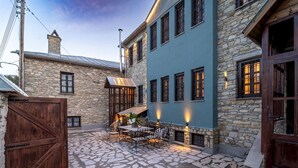 Un edificio de piedra con fachada azul, una verja de madera y un patio con mesas al aire libre.