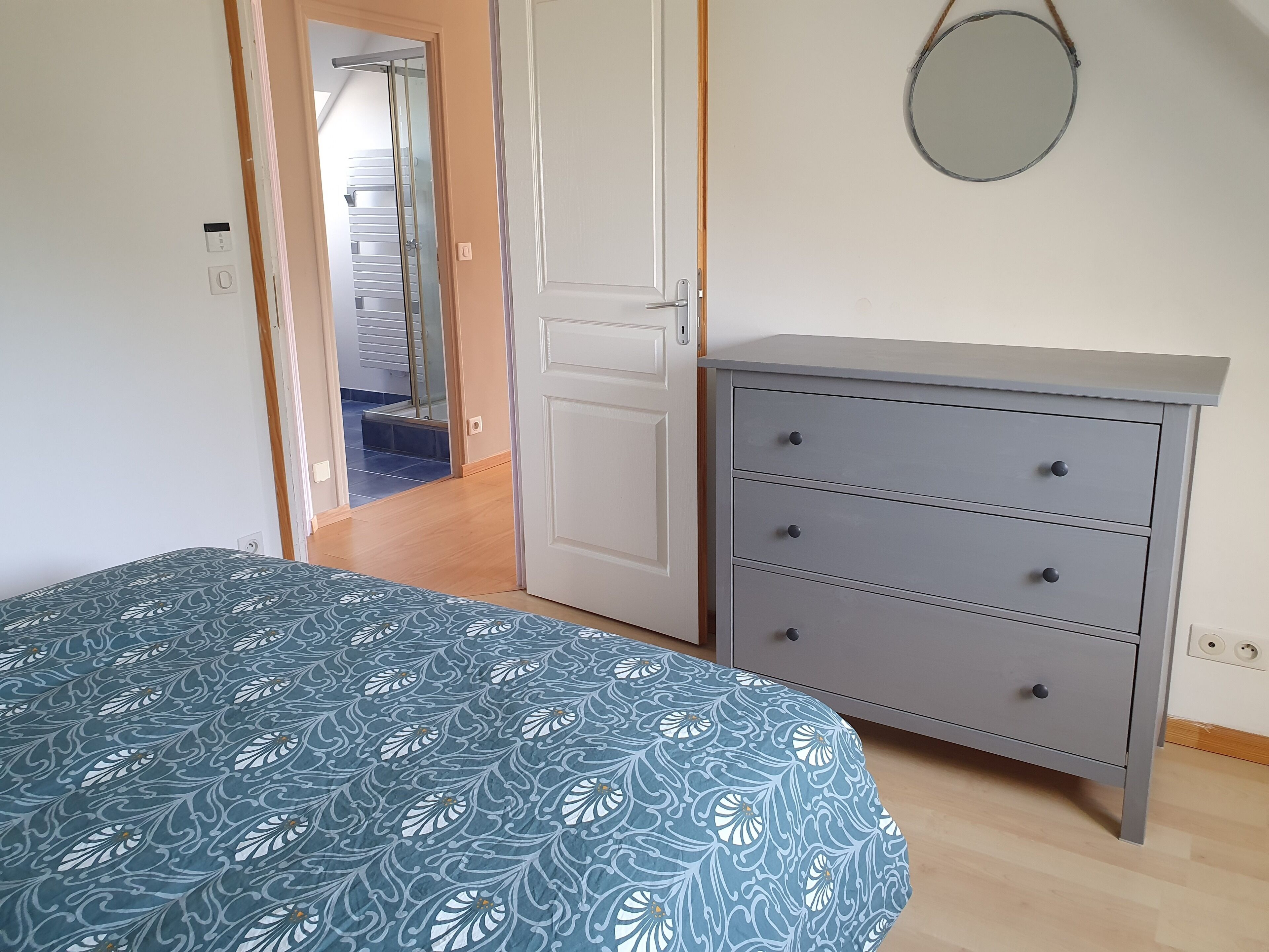 A bedroom with a bed, a dresser, a door leading to a bathroom, and a mirror on the wall.