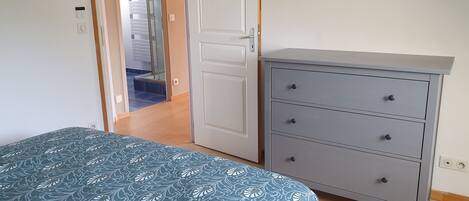A bedroom with a bed, a dresser, a door leading to a bathroom, and a mirror on the wall.