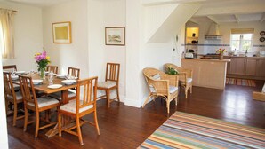 Un'area pranzo con sedie in legno e un tavolo apparecchiato per sei, una cucina con isola centrale e una scala che conduce a un piano superiore.