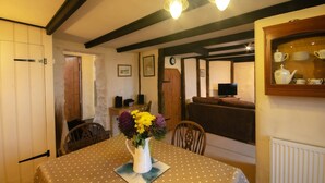 A dining area with a table set for two, a vase of flowers, and a television in the background. - Tal y Gaer Cottage, Fishguard (Trefasser)