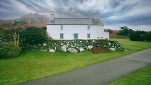A white house with a stone wall, a grassy lawn, and a mountain in the background. - Tal y Gaer Cottage, Fishguard (Trefasser)