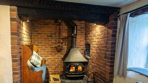 A cozy room with a brick fireplace, a wooden bench, and a window with curtains. - Tal y Gaer Cottage, Fishguard (Trefasser)